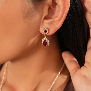 Close-up of elegant gold earrings with red teardrop stones and sparkling diamonds on a model