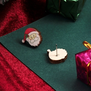 Close-up of wooden Santa Claus stud earrings on green card with festive background