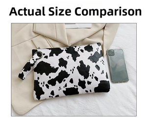 Cow print fashion envelope bag with wristlet and zipper closure next to a smartphone