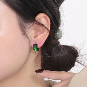 Detail of a black hoop earring with a green rectangular gemstone worn by a model