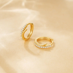 Macro shot of gold hoop earrings with sparkling clear stones on a soft beige background