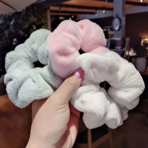 Plush faux fur scrunchies in pink, blue, and white shown in a close-up handheld view