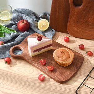 Solid ebony wood cutting board with handle hole, used as a serving tray for bread