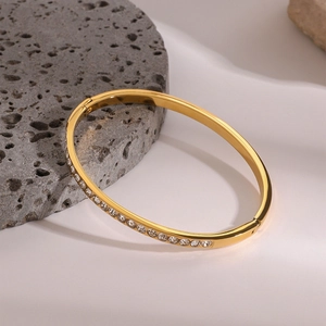 Detail view of gold stainless steel bangle with inlaid zircons on a textured stone base