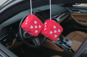 Close-up of red plush dice car charms with white embroidered hearts in luxury car interior