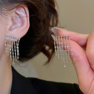 Detail of silver tassel earrings showing long beaded metal chains on a minimalist stud