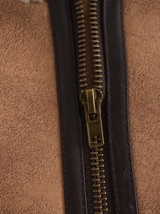 Detailed view of bronze metal zipper on tan suede vest with brown leather piping