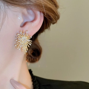 Detailed close-up of a golden starburst earring with shimmering zircon crystals on model