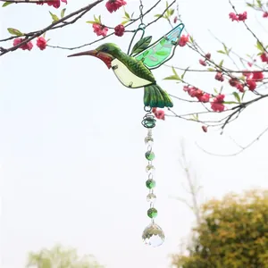 Detail of a hummingbird suncatcher with green crystal beads hanging from a tree branch
