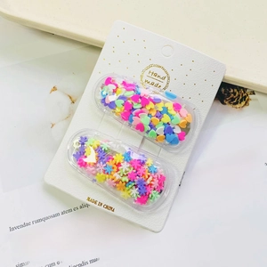 Detail view of two glitter hair clips with rainbow sequins on a white display card