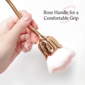 Pink rose-shaped nail dust brush with golden floral handle held by hand on white background