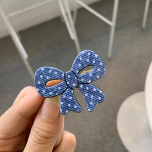 Detailed close-up of blue denim polka dot bow hair clip with gold metal duckbill clamp