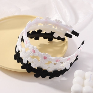 Three daisy embroidered lace headbands in white and black on a soft decorative display