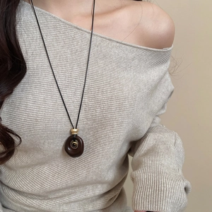 Close-up of brown resin oval pendant with gold bead on long black necklace cord