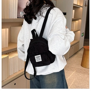 Side view of small black corduroy backpack on model showing size and texture