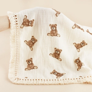 Detail of soft cotton gauze baby blanket featuring brown bear prints and tassel trim