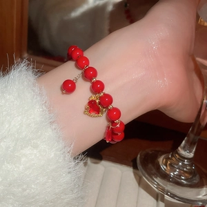 Close-up of a red glass beaded bracelet with a gold-edged heart pendant on a wrist