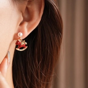 Detail of red rocking horse earring with pearl stud on model's ear in warm light