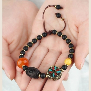 Close-up of ethnic beaded bracelet featuring black beads and colorful enamel floral accents
