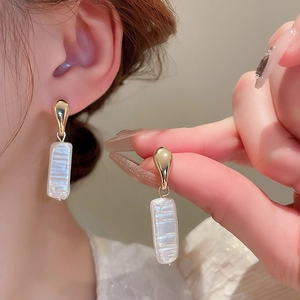 Close-up of geometric gold earrings with baroque pearl texture on model ear