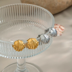 Detail of shell-shaped earrings in gold and silver finish on a glass edge at beach
