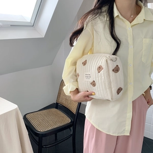 Close-up of quilted beige makeup bag featuring cute brown bear embroidery and metal D-ring