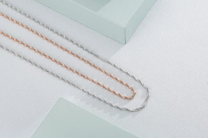 Détail de chaînes torsadées en argent et or rose sur un décor géométrique minimaliste