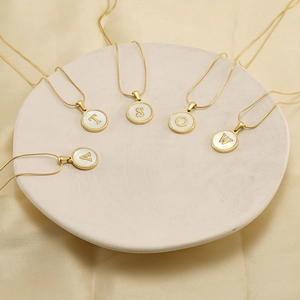 18K gold plated snake chain necklace featuring shell initial pendants on a ceramic plate