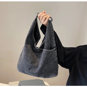 Detail of dark gray denim tote bag with external pocket shown on a shoulder