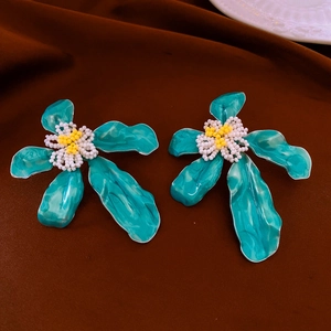 Dettaglio macro di orecchini vintage a fiore blu pavone con stami di perline fatti a mano
