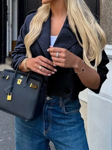 Detail der schwarzen Jacke mit Knöpfen, Goldarmbändern und einer Designer-Handtasche
