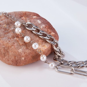 Detail of silver chain bracelet with white pearls draped over a natural brown stone