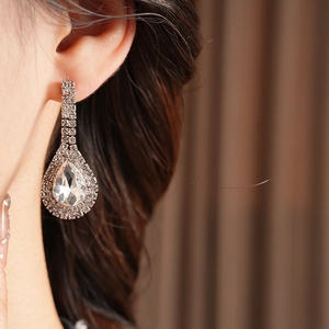 Close-up of a silver pear-shaped rhinestone earring worn on a model's ear