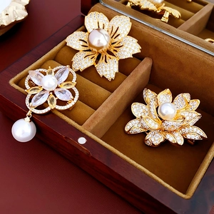 Detailed view of three gold-plated pearl flower brooches with cubic zirconia in a wooden box