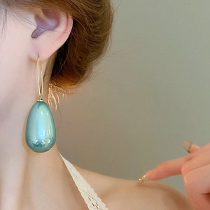 Primo piano di eleganti orecchini a goccia verde smeraldo con ganci dorati su modella