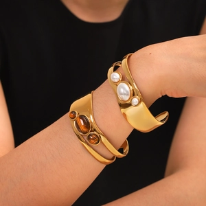Close-up of golden hollow cuff bracelets featuring natural tiger eye and white pearls
