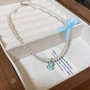 Detail of beaded pearl necklace with blue ribbon bow and transparent gummy bear charm