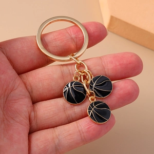 Close-up of golden metal keychain with three black enamel basketball pendants on a plain surface
