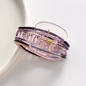 Pink and black oval claw clip with rhinestones and gold spring on a ceramic plate