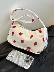 Detailed shot of cream nylon shoulder bag with red strawberry prints on a leather jacket