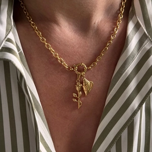 Detail of a gold necklace featuring a rose and seashell pendant on a striped shirt