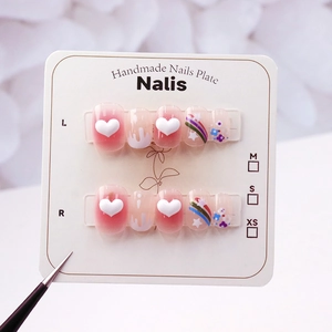 Detail of pink gradient press-on nails with 3D hearts, rainbows, and floral nail art designs