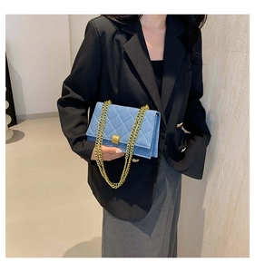 Detail of blue denim quilted handbag with gold chain strap held by model in black blazer