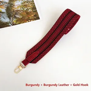 Detail of wide woven bag strap in burgundy and black with gold metal snap hooks