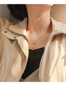Detail view of a gold coin pendant necklace worn by a model in a natural setting