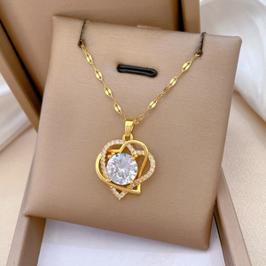 Macro detail of gold double-heart necklace with large central crystal on beige cushion