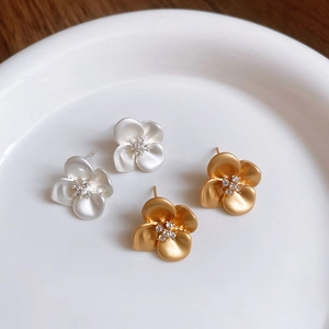 Detailed top view of gold and silver flower stud earrings with zircon in a white dish