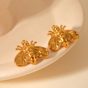 Macro shot of 18K gold plated bee stud earrings on a textured off-white tray