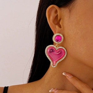 Detail of pink resin heart earrings with rhinestone trim worn by a female model