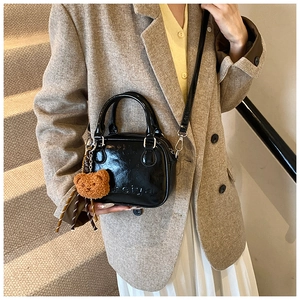 Detail of mini black crossbody bag with meiya relief and brown plush bear charm